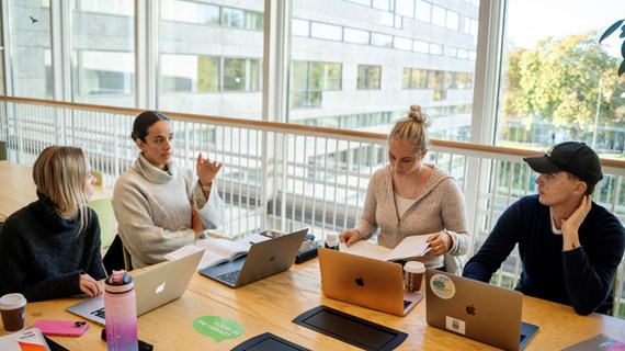 En grupp människor som sitter runt ett bord med bärbara datorer.