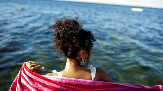 Person i badkläder tittar ut över havet och torkar sig över ryggen med en handduk.