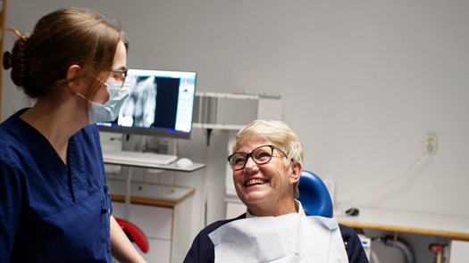 Äldre patient i tandläkarstol ler mot tandvårspersonal.