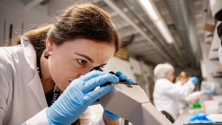En person i ett laboratorium tittar genom ett mikroskop.