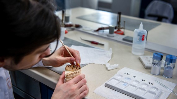 Student från tandteknikerutbildningen målar tandersättningar.