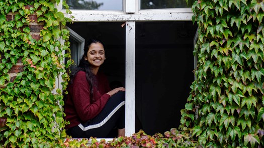 Student sitter i fönster till sin bostad och tittar in i kameran.