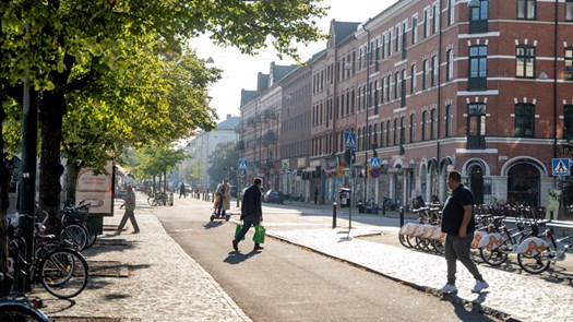 En grupp människor som går längs en gata bredvid höga byggnader.