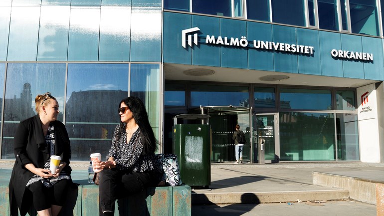 Studenter fikar i solen utanför universitetet.
