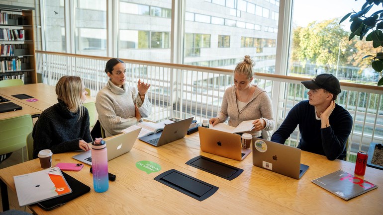 En grupp människor som sitter runt ett bord med bärbara datorer.