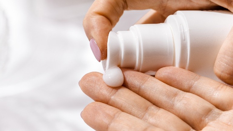 Image shows someone dispensing a cream on their hands