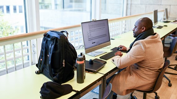 Student jobbar framför dator i universitetsbiblioteket.