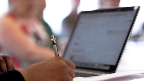 Hand som antecknar framför laptop.