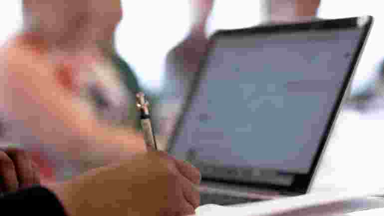 Person taking notes in front of a laptop.