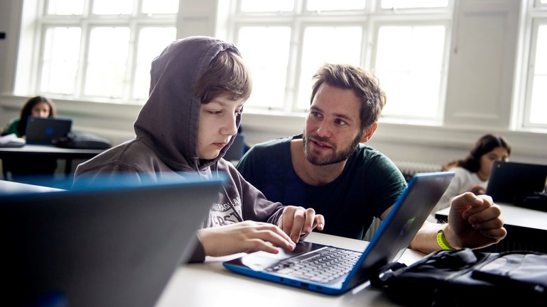 Lärare hjälper elev som skriver på dator.