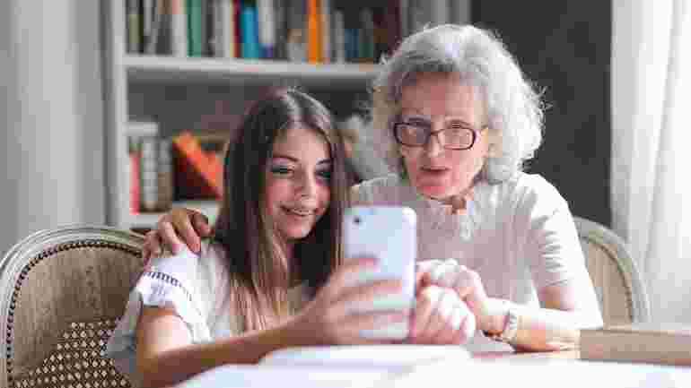 Ung person och äldre dam tittar på en mobiltelefon tillsammans.