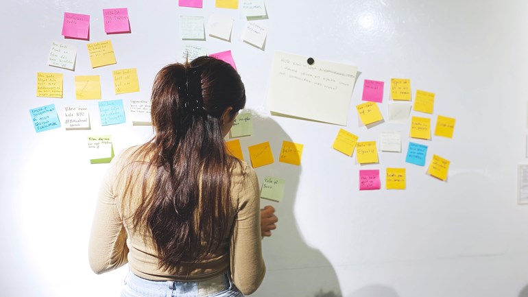 Ung praktikant som sorterar postit-lappar på en whiteboard