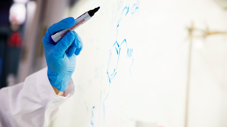 Närbild på hand med skyddshandskar som skriver med whiteboard-penna.