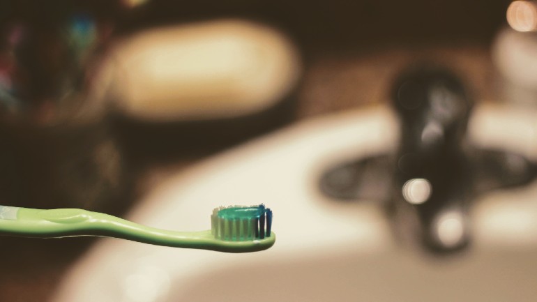Close up of a toothbrush against the backdrop of a blurred bathroom basin