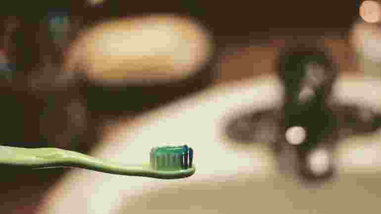 Close up of a toothbrush against the backdrop of a blurred bathroom basin