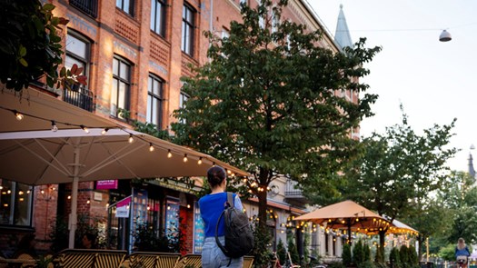 En person går längs en gata bredvid höga byggnader.