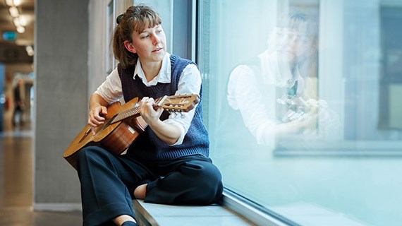 Person som sitter i fönster och spelar gitarr.