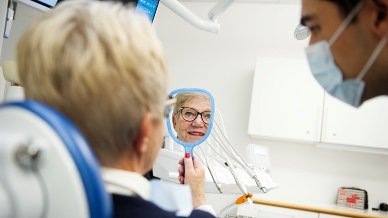 Patient i behandlingsrum på tandvårdskliniken ser sig i en handspegel.