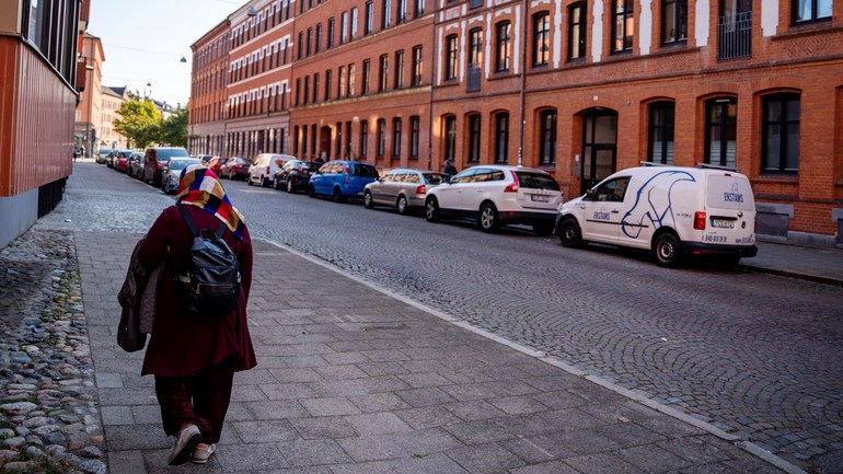 En person går längs en gata bredvid höga byggnader